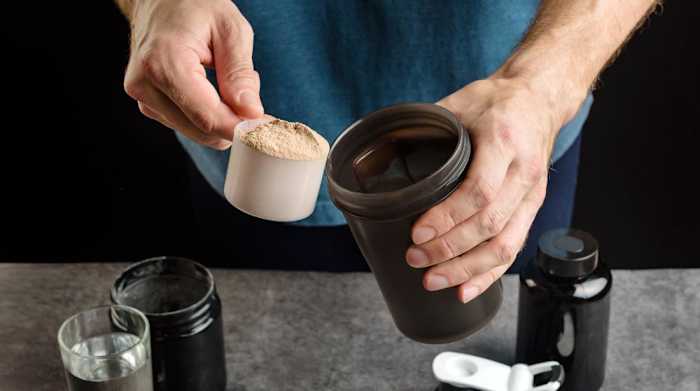 Man scooping protein powder into a shaker bottle